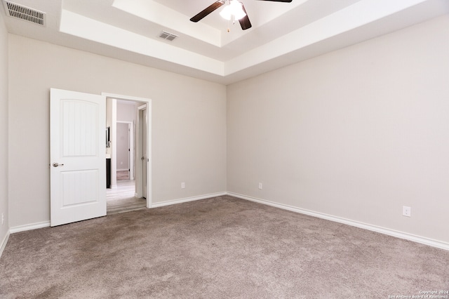 empty room with ceiling fan, a raised ceiling, and carpet flooring