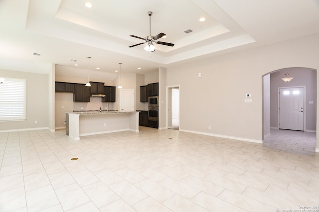 unfurnished living room with ceiling fan, a raised ceiling, and light tile patterned floors