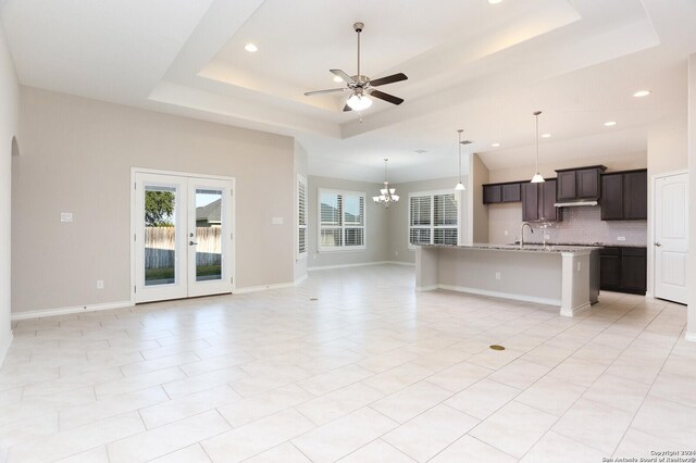 kitchen featuring an island with sink, sink, tasteful backsplash, a tray ceiling, and ceiling fan with notable chandelier