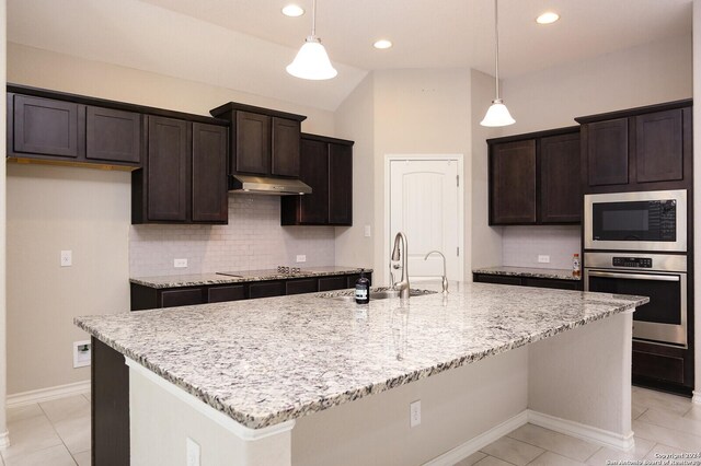 kitchen with appliances with stainless steel finishes, hanging light fixtures, vaulted ceiling, and an island with sink