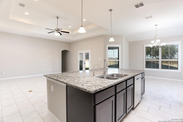 kitchen with ceiling fan with notable chandelier, light stone countertops, a tray ceiling, dark brown cabinetry, and sink