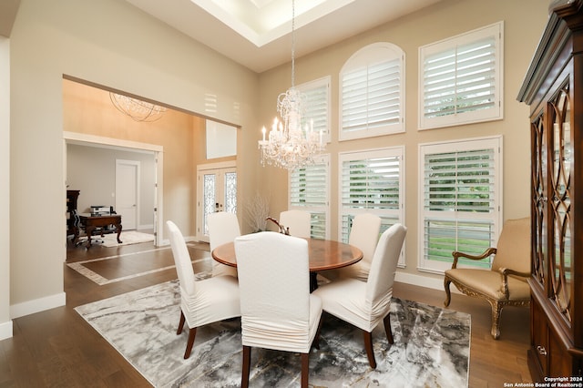 dining area with dark hardwood / wood-style flooring, an inviting chandelier, and a towering ceiling