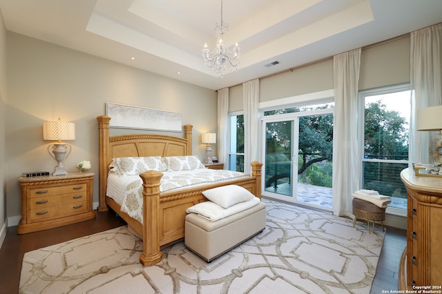 bedroom with a tray ceiling, light hardwood / wood-style floors, an inviting chandelier, and access to outside