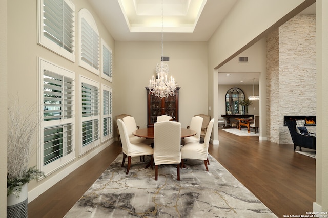 dining room with an inviting chandelier, a fireplace, hardwood / wood-style flooring, a towering ceiling, and a tray ceiling