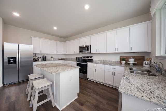 kitchen with stainless steel appliances, sink, white cabinets, a center island, and dark wood-type flooring