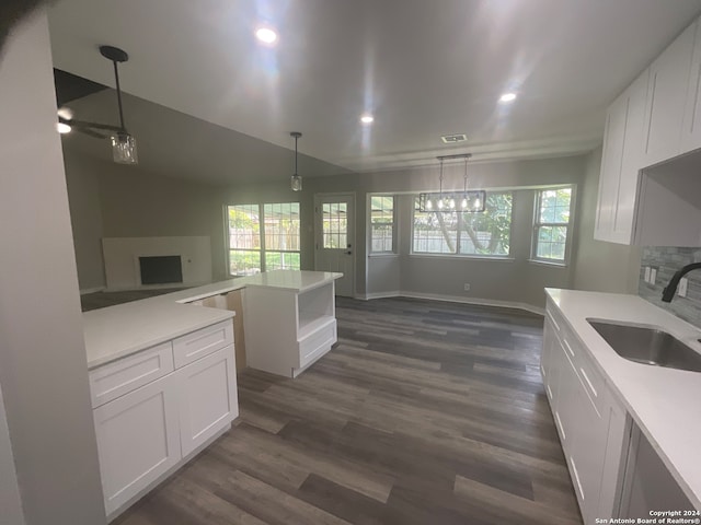 kitchen with a stone fireplace, white cabinetry, sink, and decorative light fixtures