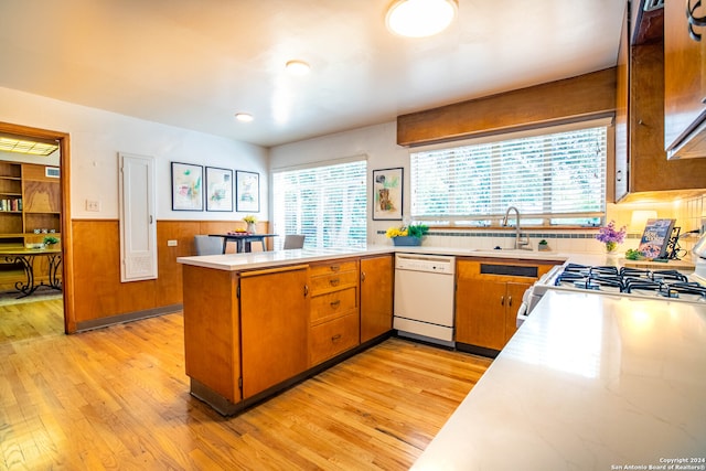 kitchen featuring dishwasher, stove, wooden walls, light wood-type flooring, and kitchen peninsula