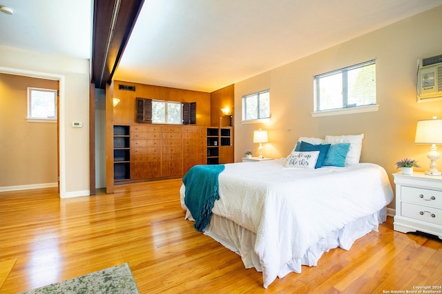 bedroom featuring beamed ceiling, multiple windows, light wood-style floors, and baseboards