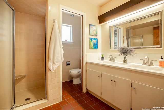 bathroom with tile patterned floors, toilet, vanity, a shower with shower door, and tile walls