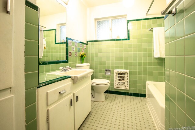 full bathroom with heating unit,  shower combination, toilet, vanity, and tile walls