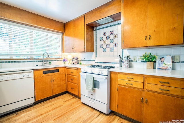 kitchen with light wood finished floors, tasteful backsplash, light countertops, white appliances, and a sink