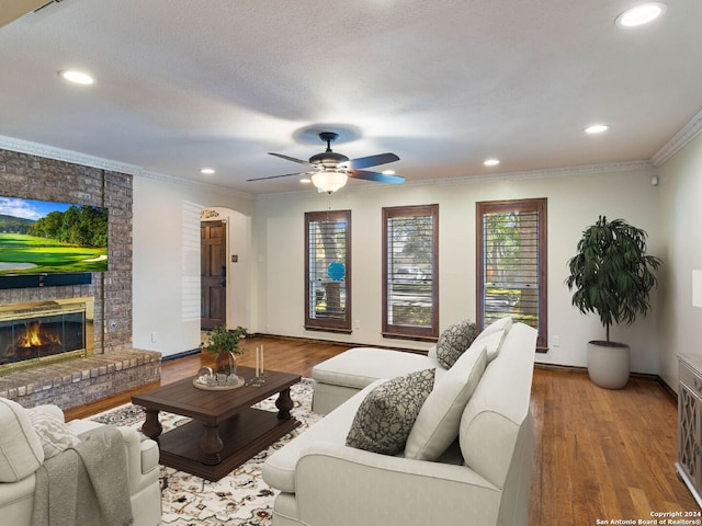 living room featuring ceiling fan, a brick fireplace, crown molding, a textured ceiling, and hardwood / wood-style flooring