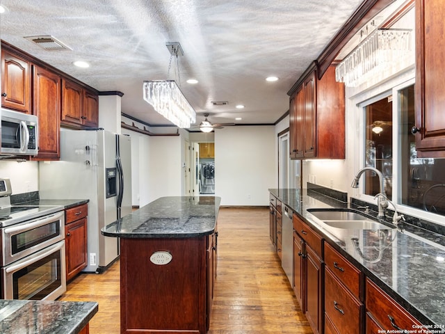 kitchen with sink, light wood-type flooring, appliances with stainless steel finishes, decorative light fixtures, and a kitchen island