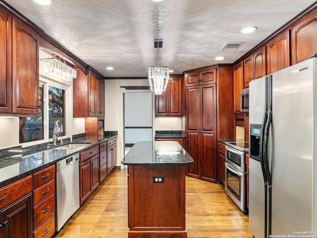 kitchen with dark stone counters, light hardwood / wood-style floors, a textured ceiling, a kitchen island, and stainless steel appliances