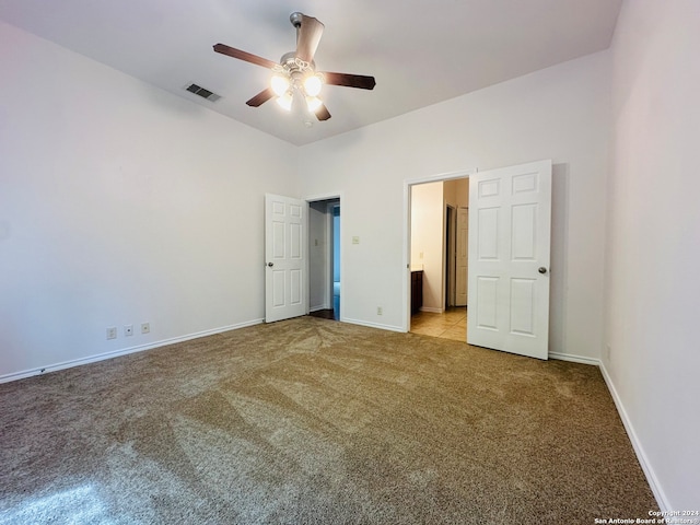 unfurnished bedroom featuring ceiling fan, light colored carpet, and ensuite bath