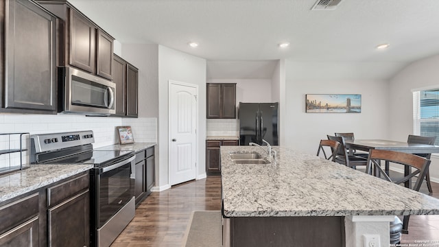 kitchen featuring dark hardwood / wood-style floors, tasteful backsplash, sink, stainless steel appliances, and a center island with sink