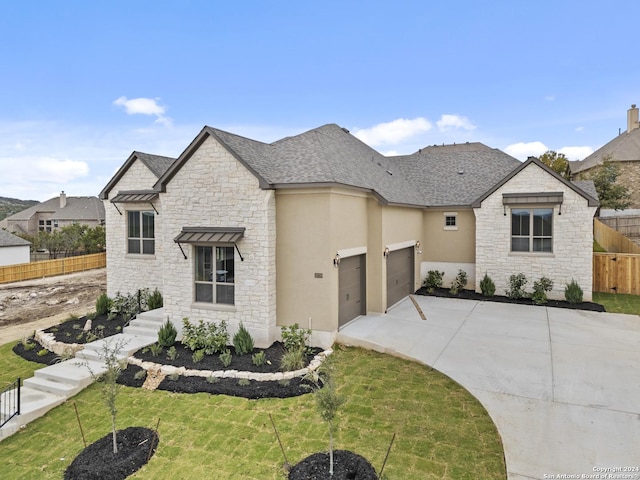 french country home with a front yard, concrete driveway, fence, and stucco siding