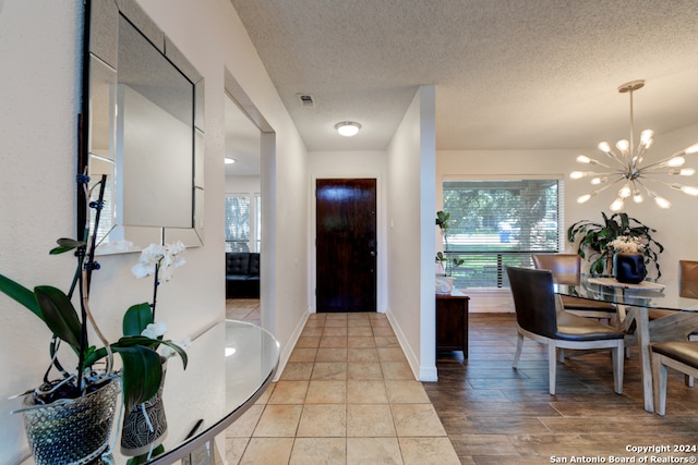 tiled entrance foyer featuring a textured ceiling and a chandelier