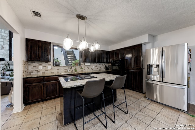 kitchen featuring decorative light fixtures, tasteful backsplash, black appliances, light stone countertops, and a kitchen island