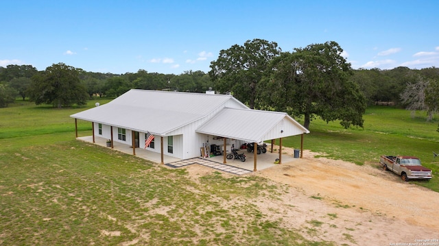 view of front of home featuring dirt driveway, a view of trees, metal roof, a front lawn, and a carport