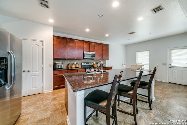 kitchen with a kitchen bar, sink, light tile patterned floors, stainless steel appliances, and a center island with sink