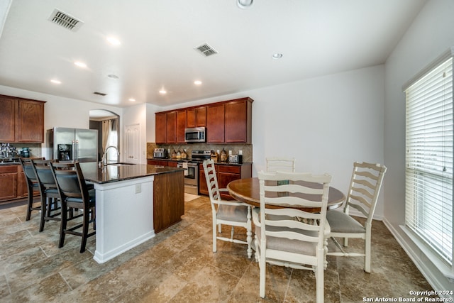 kitchen featuring light tile patterned flooring, sink, appliances with stainless steel finishes, decorative backsplash, and a kitchen island with sink