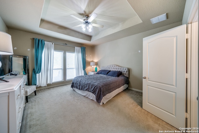 bedroom with ceiling fan, light carpet, and a tray ceiling