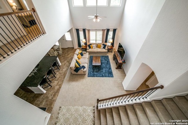 carpeted living area featuring a towering ceiling, ceiling fan, and stairway