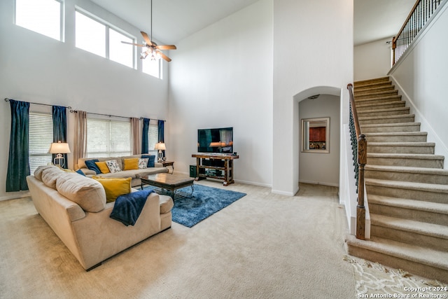 carpeted living room featuring ceiling fan and a towering ceiling