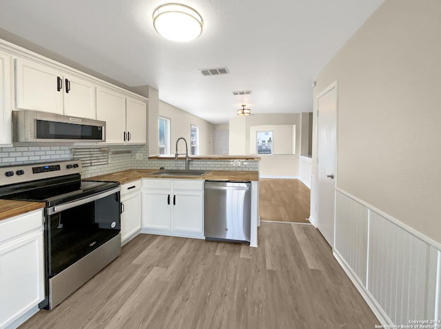 kitchen with stainless steel appliances, visible vents, a sink, wood counters, and a peninsula