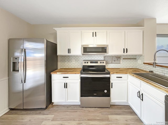 kitchen with appliances with stainless steel finishes, light wood-type flooring, butcher block counters, and a sink