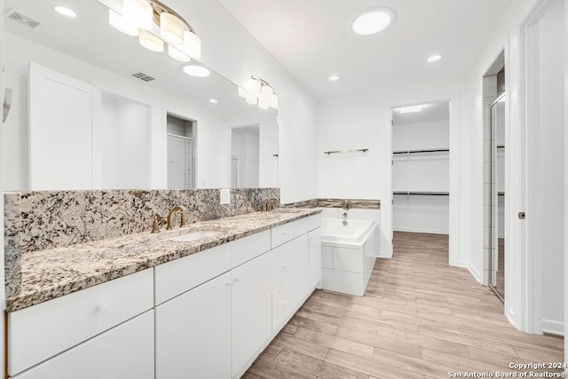 full bathroom with visible vents, a walk in closet, a sink, and wood finished floors