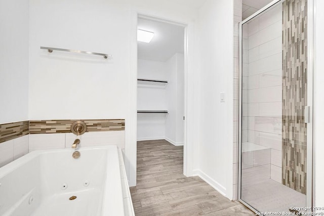 full bathroom featuring baseboards, a tub with jets, wood finished floors, a spacious closet, and a shower stall