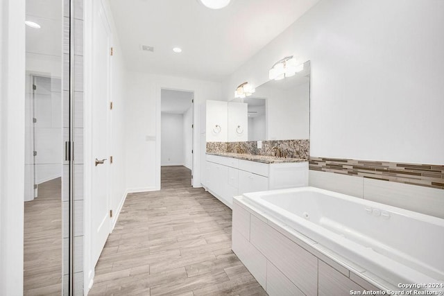 bathroom featuring a whirlpool tub, wood finished floors, vanity, and baseboards