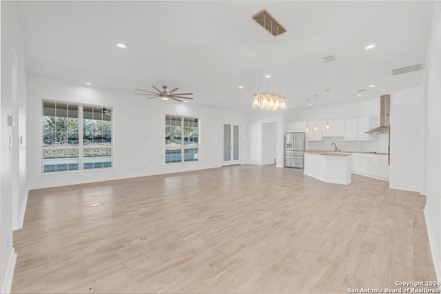 unfurnished living room featuring ceiling fan with notable chandelier and light hardwood / wood-style flooring