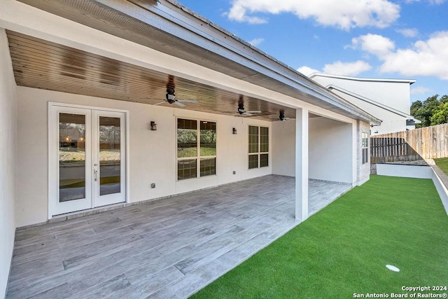 back of property with french doors, stucco siding, a lawn, ceiling fan, and fence