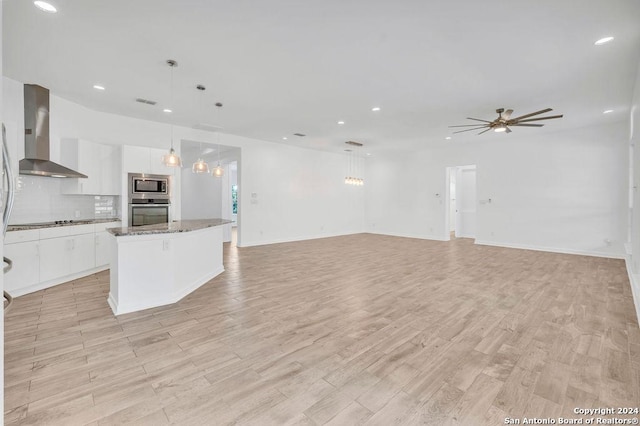 kitchen featuring stainless steel appliances, backsplash, white cabinets, a kitchen island, and wall chimney exhaust hood