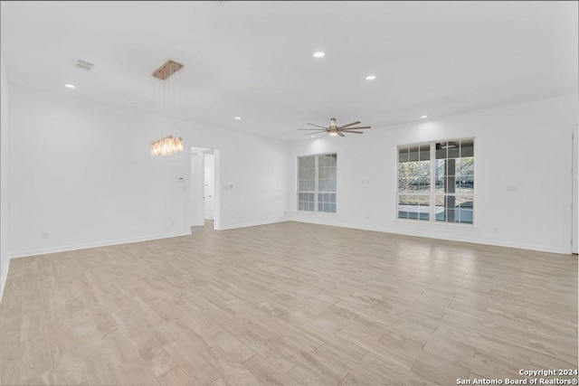 unfurnished living room with recessed lighting, ceiling fan with notable chandelier, visible vents, baseboards, and light wood-type flooring