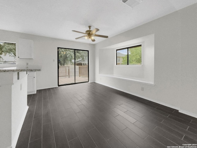 unfurnished living room featuring a ceiling fan, baseboards, visible vents, and dark wood-type flooring