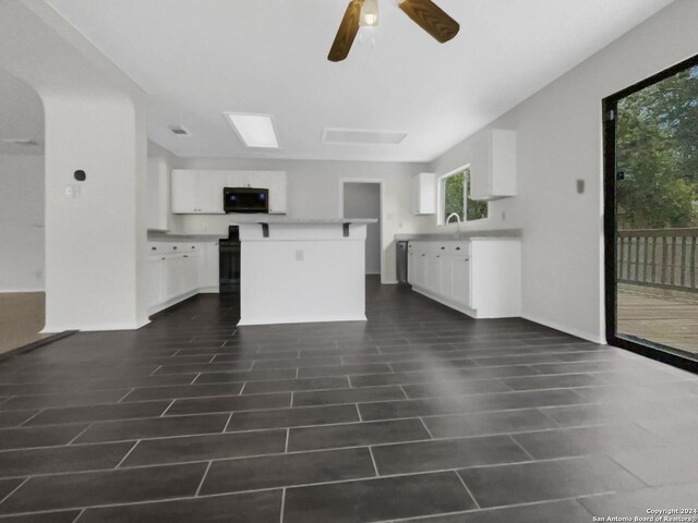 kitchen with white cabinets, a center island, dark tile patterned floors, sink, and ceiling fan