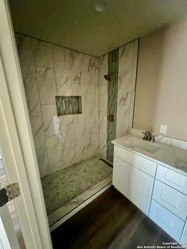 bathroom with hardwood / wood-style floors, a tile shower, and vanity