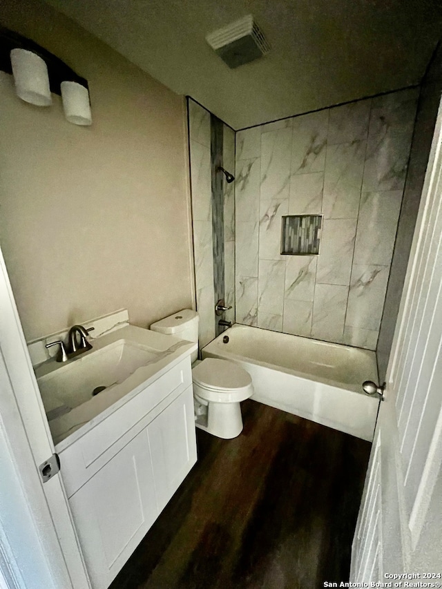 full bathroom featuring wood-type flooring, toilet, tiled shower / bath combo, and vanity