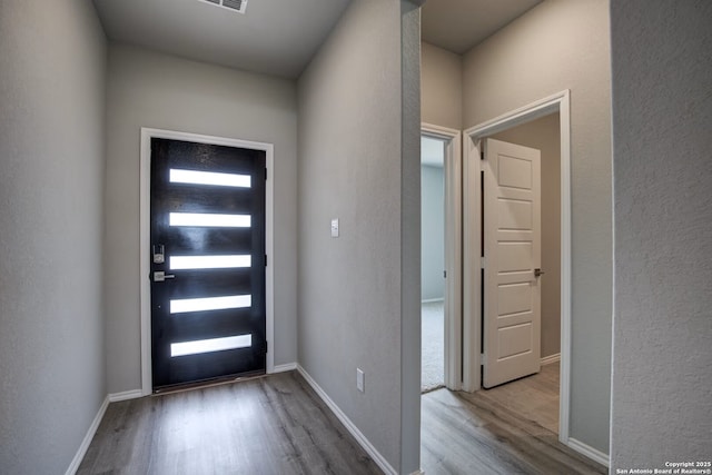 foyer entrance with light wood finished floors, baseboards, and a textured wall