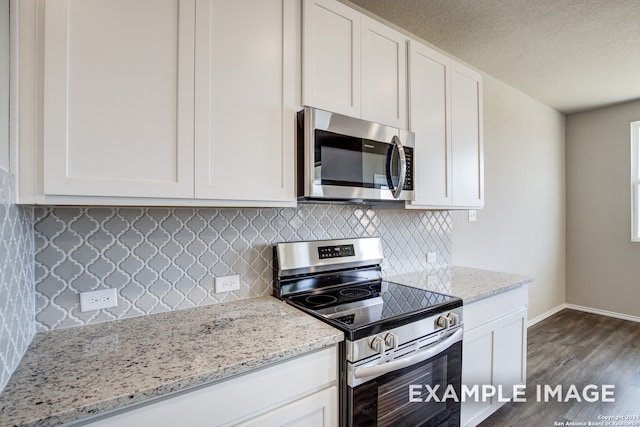 kitchen featuring appliances with stainless steel finishes, dark wood-style flooring, white cabinetry, and light stone counters