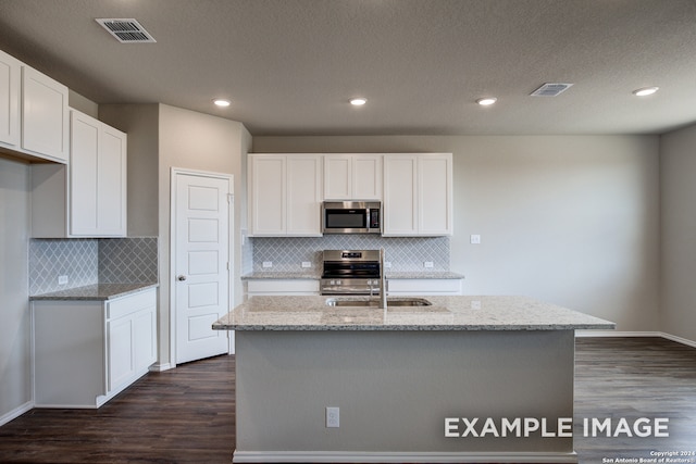 kitchen featuring a center island with sink, stainless steel appliances, visible vents, white cabinetry, and light stone countertops