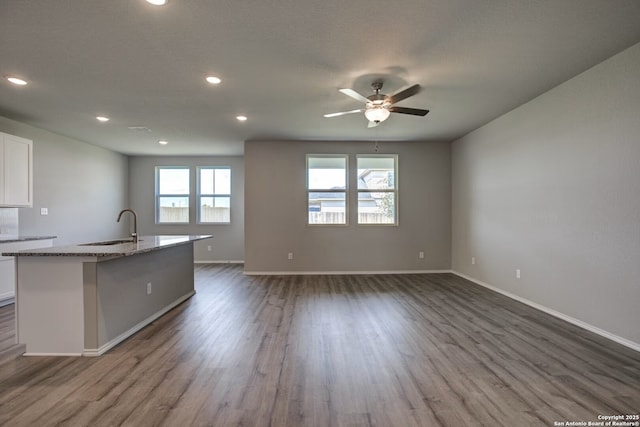 kitchen with light stone counters, open floor plan, a kitchen island with sink, white cabinetry, and a sink