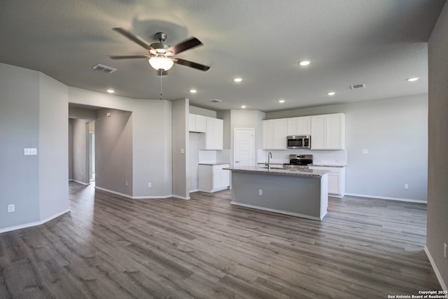 kitchen with appliances with stainless steel finishes, an island with sink, light stone countertops, and white cabinets