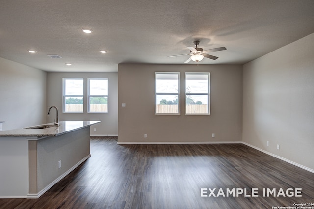 kitchen featuring visible vents, dark wood-type flooring, a sink, an island with sink, and light stone countertops