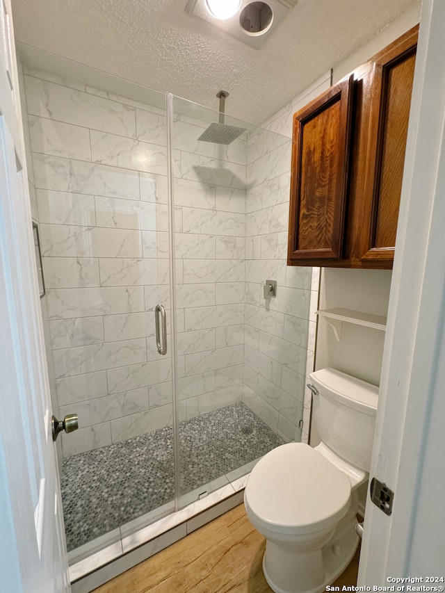 bathroom with toilet, a shower with door, a textured ceiling, and wood-type flooring