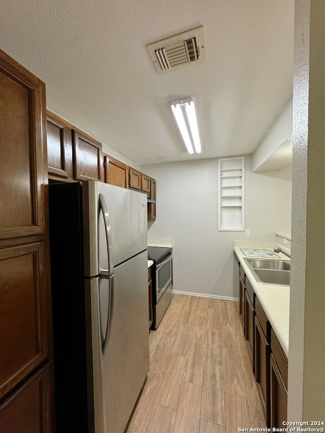 kitchen with sink, stainless steel appliances, light hardwood / wood-style floors, and a textured ceiling